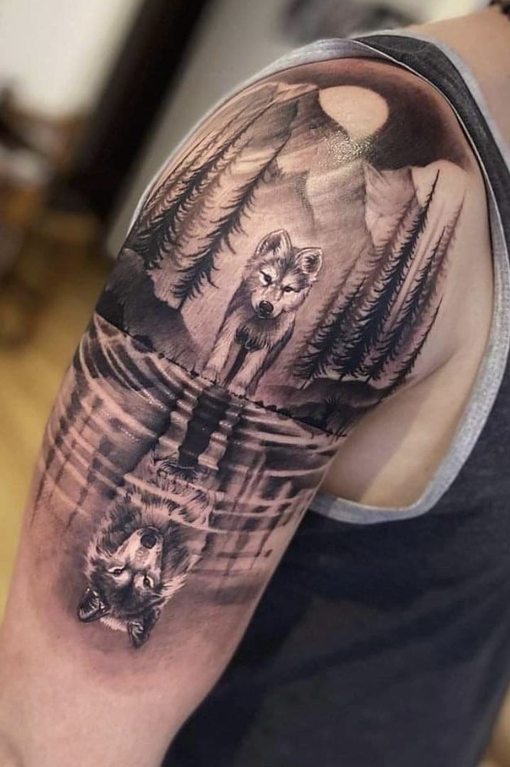 a man's arm with a wolf and forest scene tattoo on the left shoulder