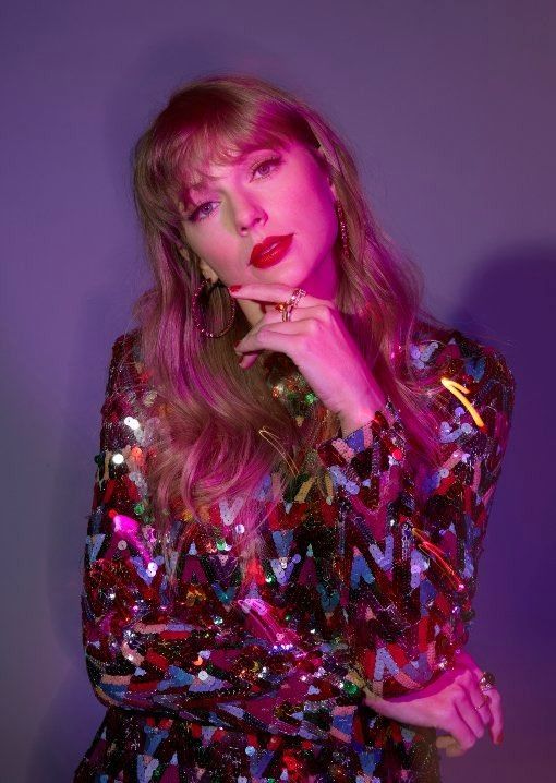 a woman with pink hair wearing a sequin dress and holding her hand on her chin