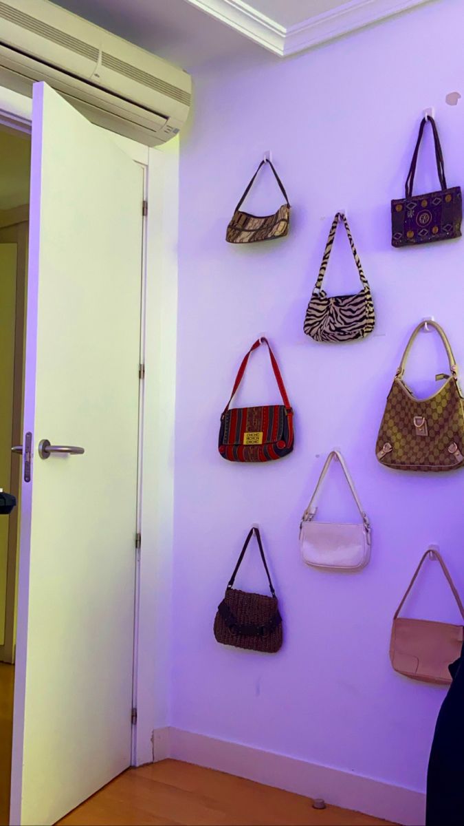 purses are hanging on the wall in front of a purple wall with white doors