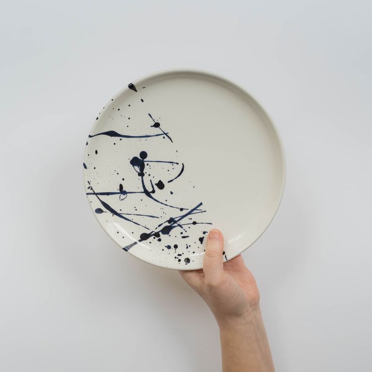 a hand holding a white plate with black paint splattered on the bottom and sides