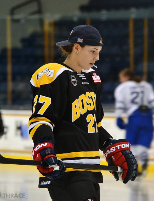 a female hockey player on the ice with her stick in hand and wearing a black hat