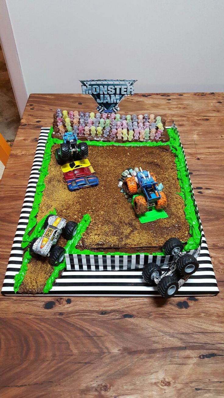 a monster truck themed birthday cake on a table with toy trucks in the dirt and grass