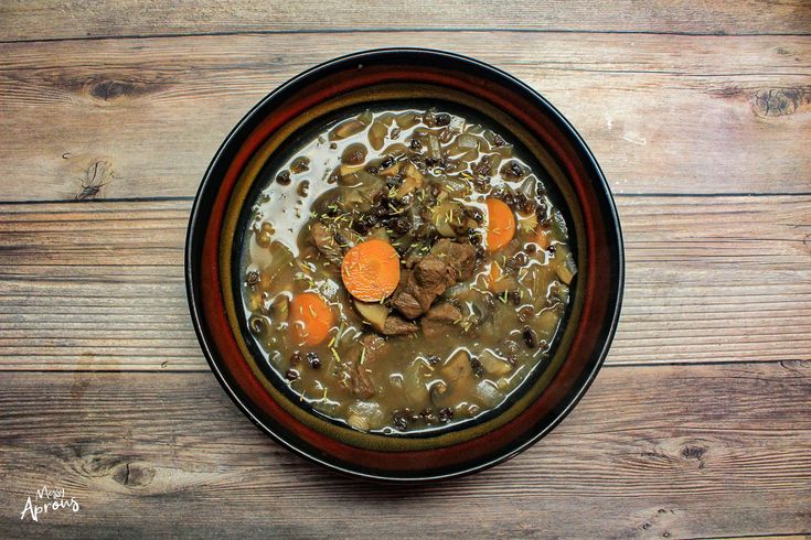 a bowl of soup with carrots, meat and broth on a wooden table