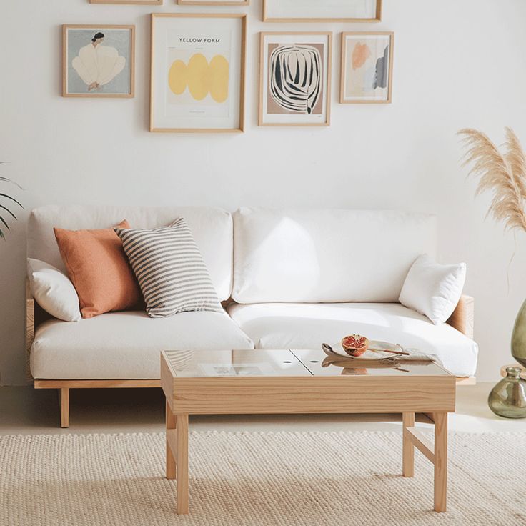 a living room with white couches and pillows on the coffee table in front of it