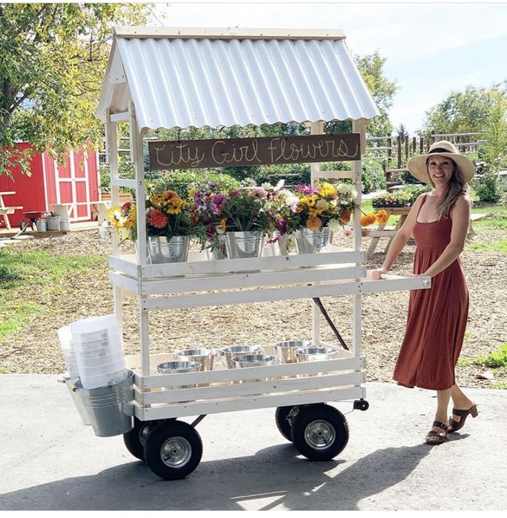 a woman standing next to a cart filled with flowers