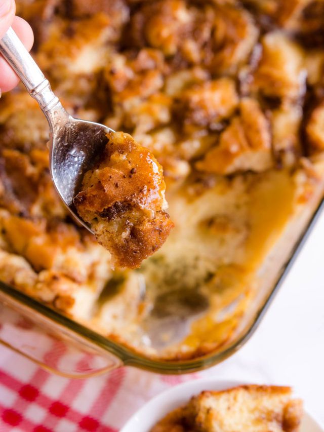 a person holding a spoon over a casserole dish with bread and pudding in it