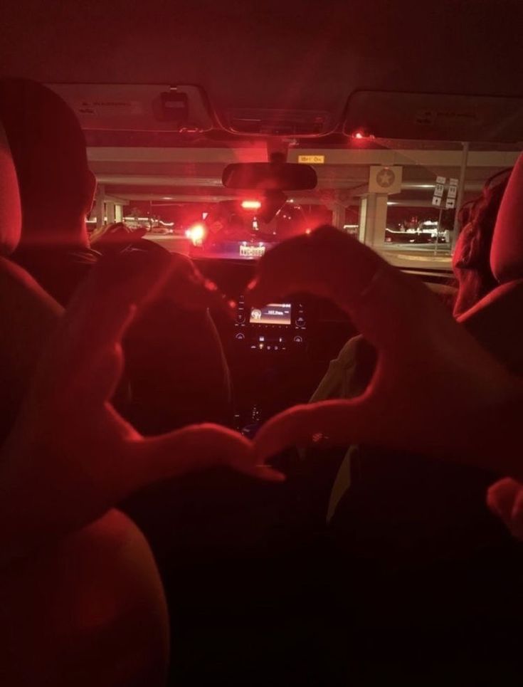 two people sitting in the back seat of a car making a heart with their hands