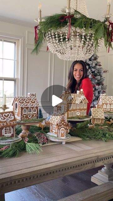 a woman standing in front of a table filled with gingerbread houses and christmas decorations