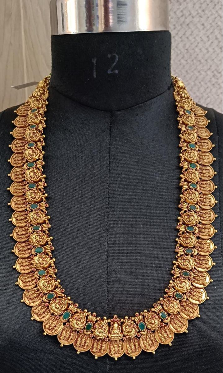 an elaborate gold necklace with green stones on display in front of a black mannequin