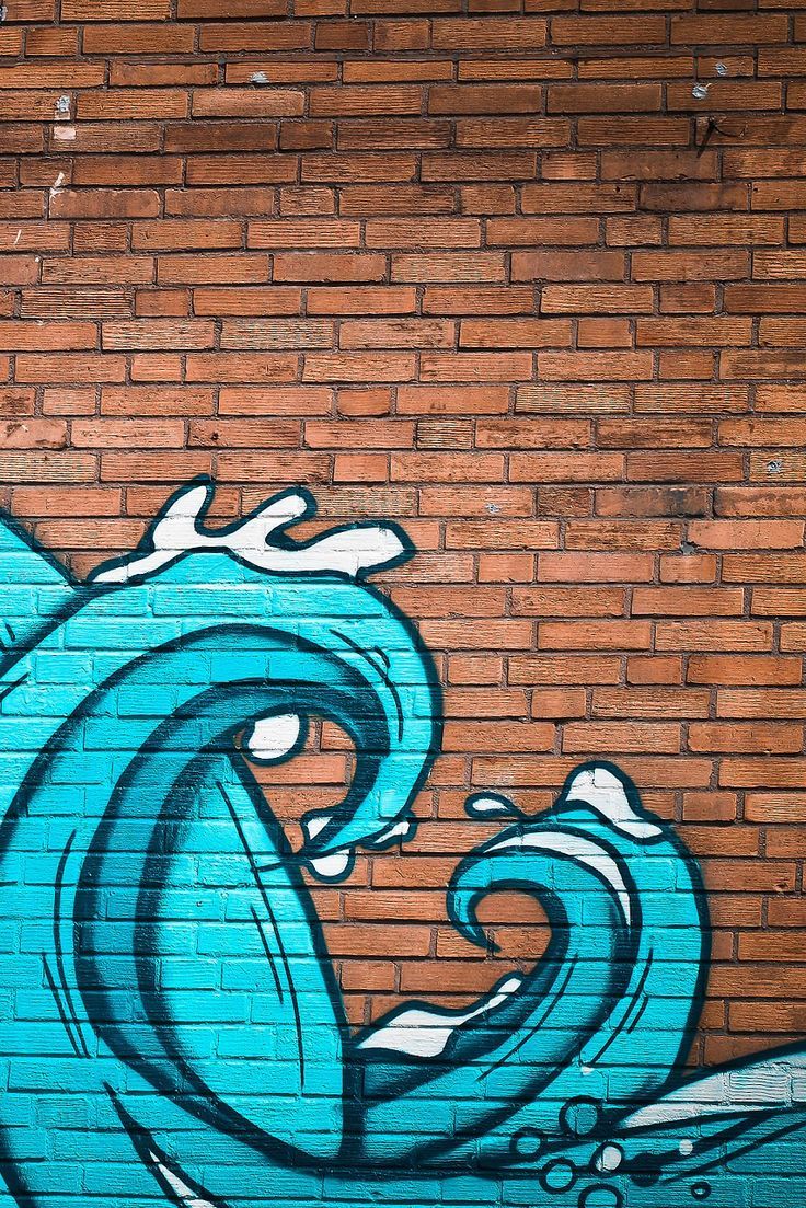 a brick wall with graffiti on it and a blue wave painted on the side by hand