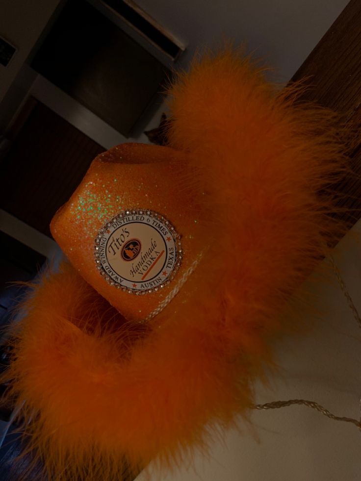 an orange hat with feathers hanging from it's side on a counter top next to a mirror