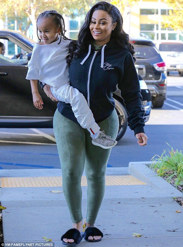 a woman carrying a child while walking down the sidewalk in her green leggings