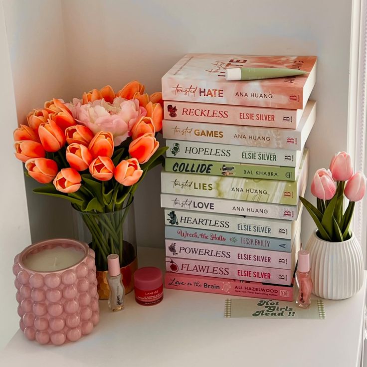 a stack of books sitting on top of a white shelf next to a vase filled with flowers