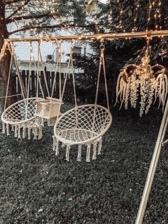 some white chairs hanging from a tree with string lights in the back ground and on top of them