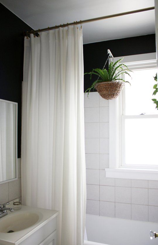 a white bath tub sitting under a window next to a plant in a hanging basket