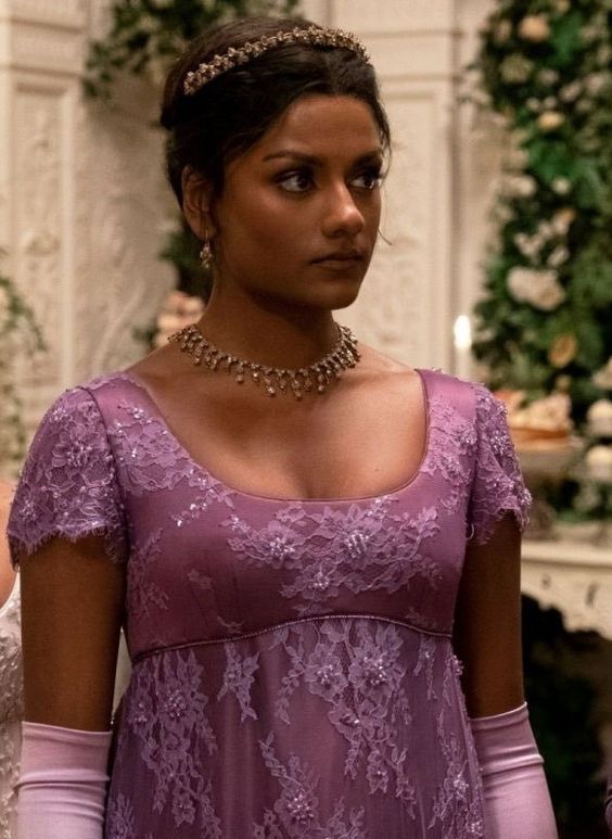 a woman in a purple dress standing next to another woman wearing a tiara and gloves