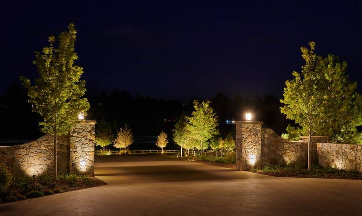 an entrance to a home at night with lights on and trees lining the driveway area