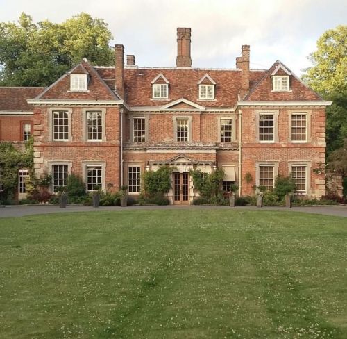 a large brick building with lots of windows on the front and side of it, surrounded by lush green grass