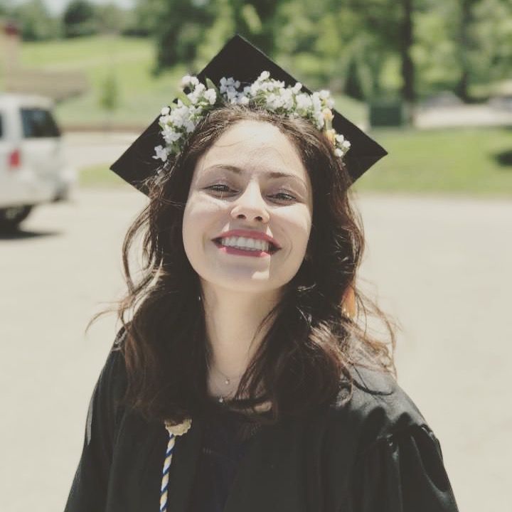 a woman wearing a graduation cap and gown with flowers in her hair smiles at the camera