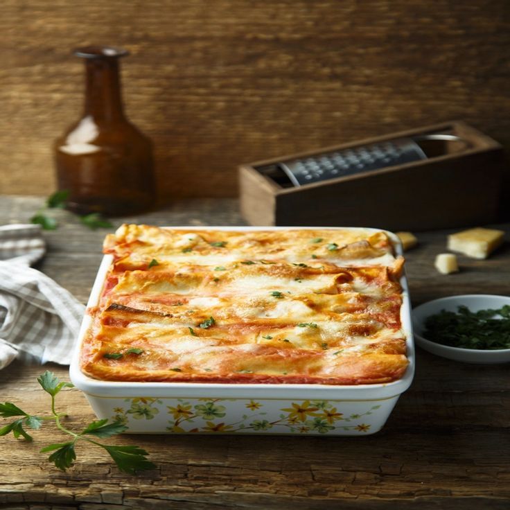 a casserole dish is shown on a wooden table with herbs and other ingredients