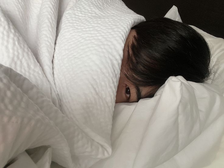 a woman is hiding under the covers in bed with her head tucked between two pillows