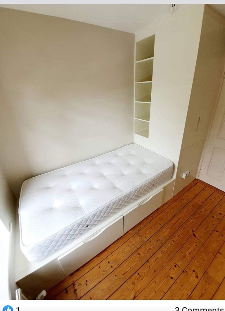 a white bed sitting in the corner of a room next to a book shelf and door