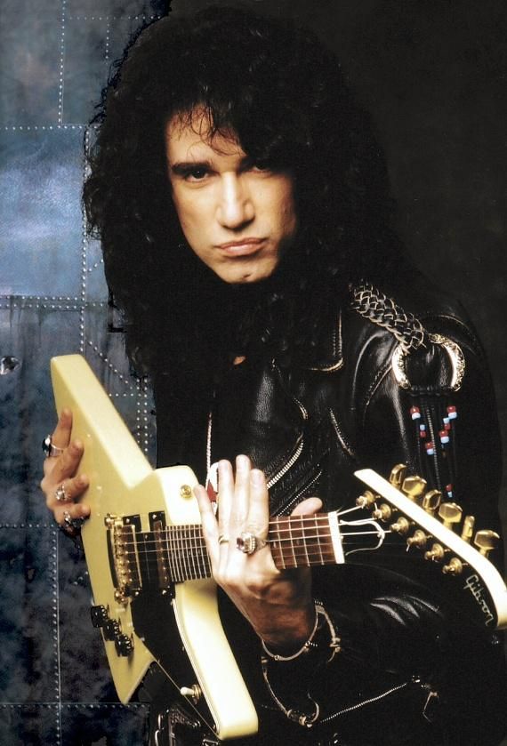 a man with long black hair is holding a yellow guitar and posing for the camera