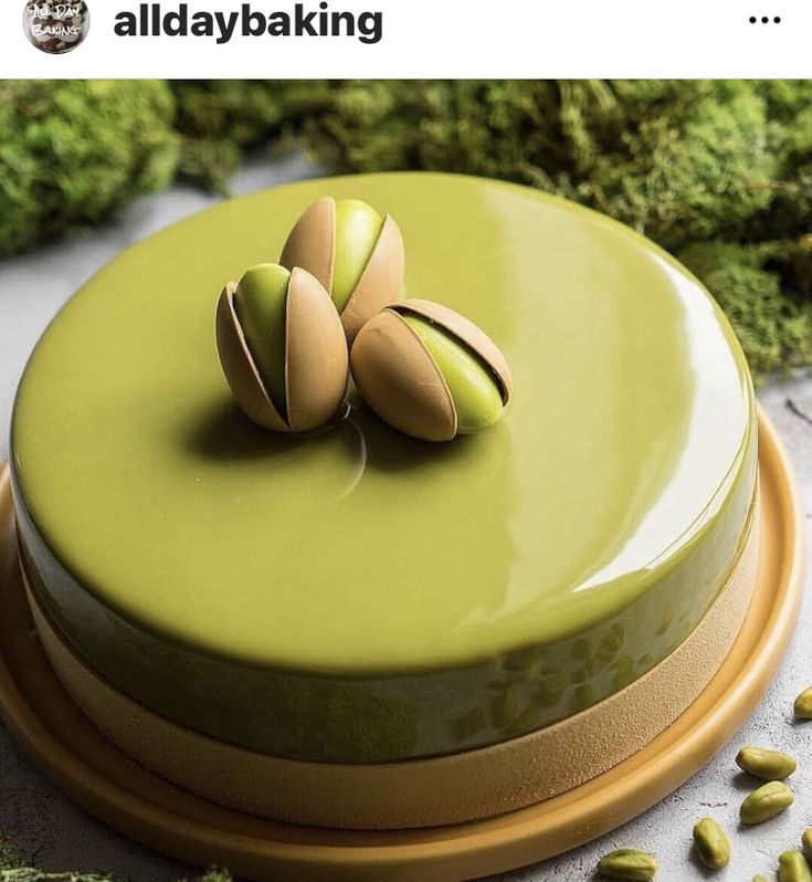 a green cake with pistachios on top sitting on a platter surrounded by greens