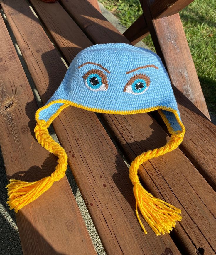 a crocheted blue and yellow hat sitting on top of a wooden bench