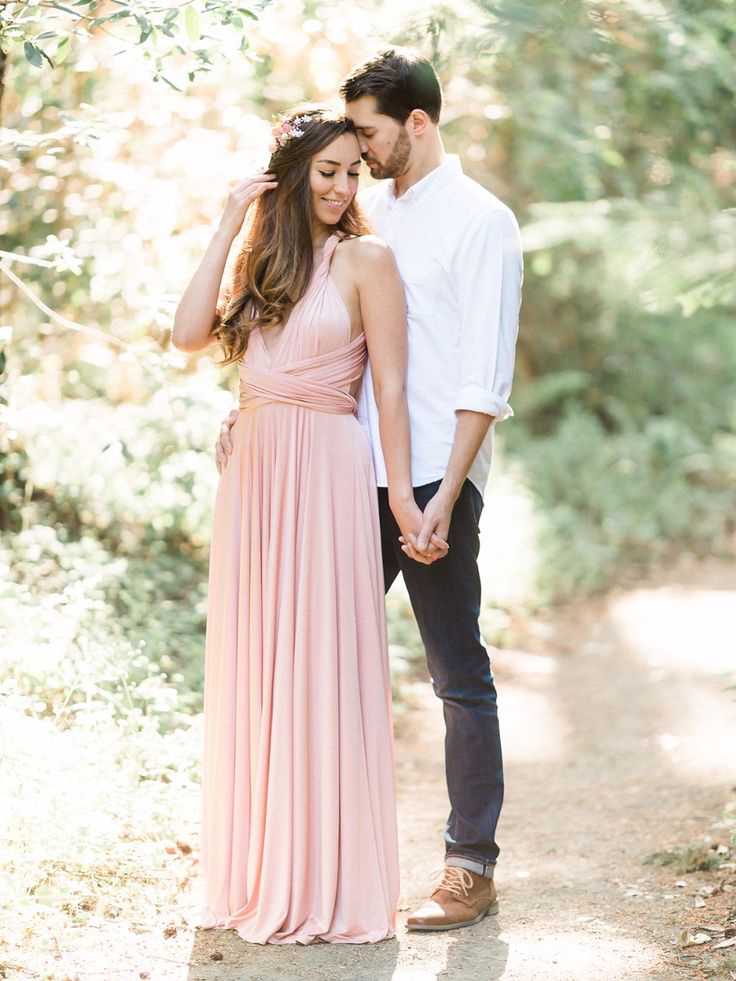 a man and woman holding hands while standing on a dirt path in the woods with trees