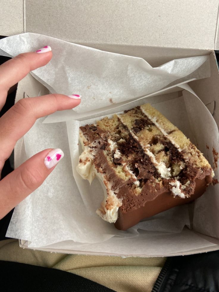 a piece of cake sitting in a white paper box with someone's hand on it