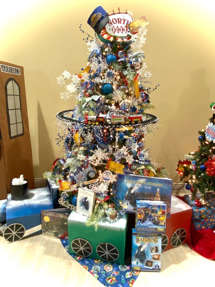 a christmas tree with train decorations and presents under it on a table in front of a wall