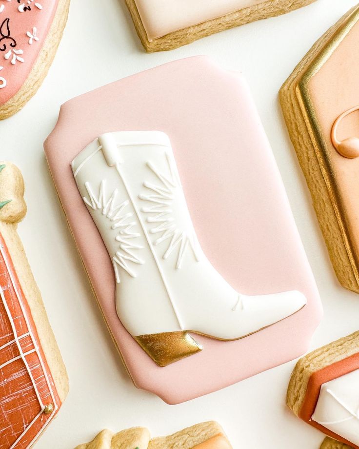 decorated cookies with white boots and gold trim on pink tray next to cookie cutters