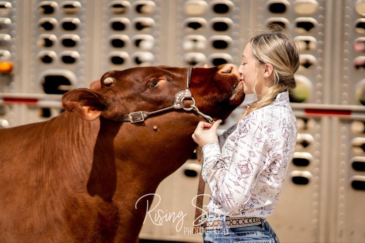 a woman is kissing the nose of a brown cow