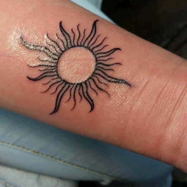 a small sun tattoo on the wrist is shown in black ink, and it appears to be an intricate design