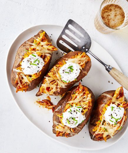 four baked potatoes on a white plate with a spatula next to them and a cup of coffee