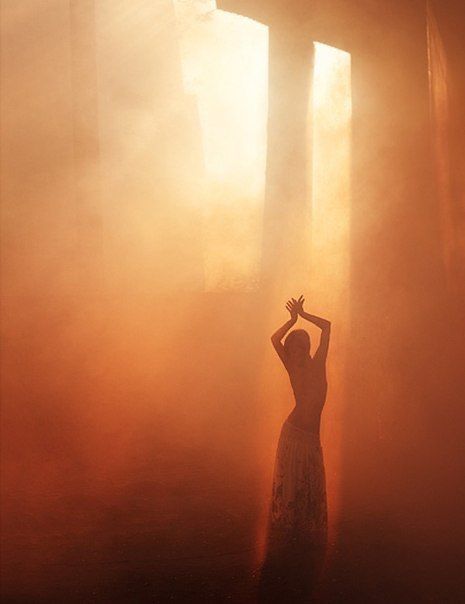 a woman standing in the middle of a foggy forest with her arms raised up