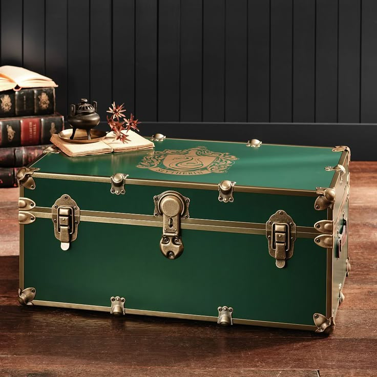 a green trunk sitting on top of a wooden floor next to a pile of books