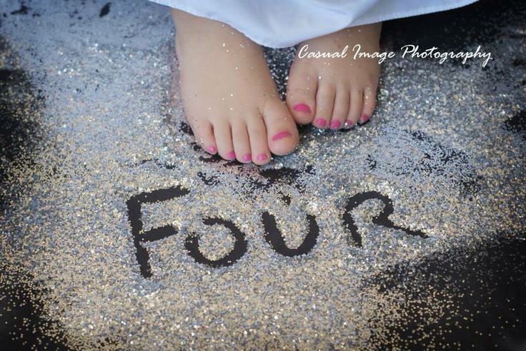 a child's feet in sand with the word four written on it and glitters all around them