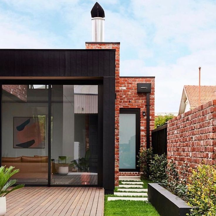 a house with brick walls and wooden decking next to grass covered garden area in front of it