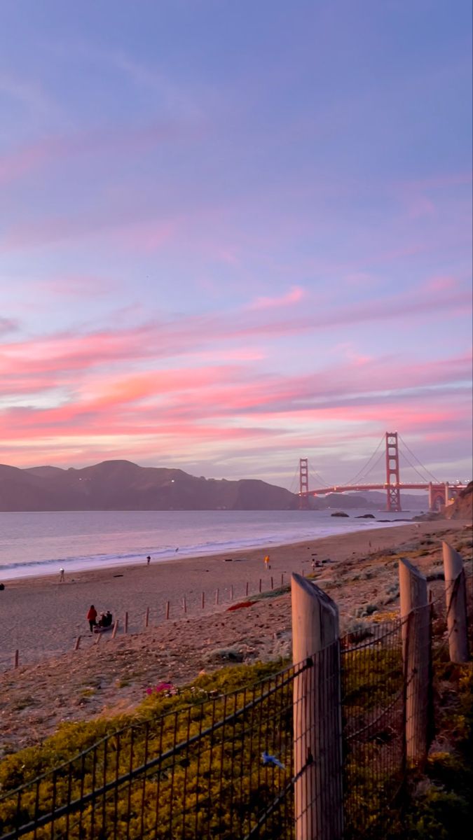 A sunset at the beach with Golden Gate Bridge in the background San Francisco Sunset, San Francisco Aesthetic, San Francisco Wallpaper, Presidio San Francisco, Pch Road Trip, Pastel Nature, Dream Places To Visit, Sf Wallpaper, California Coast Road Trip