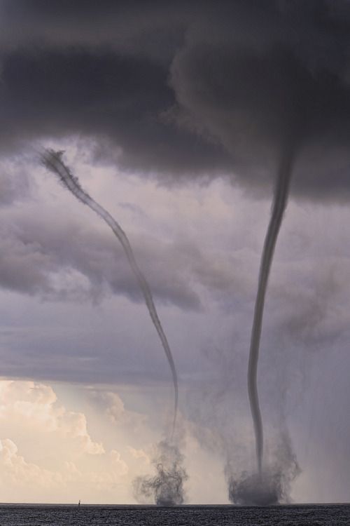 two jets are flying in the sky near some water and storm clouds, while another jet is coming up behind them