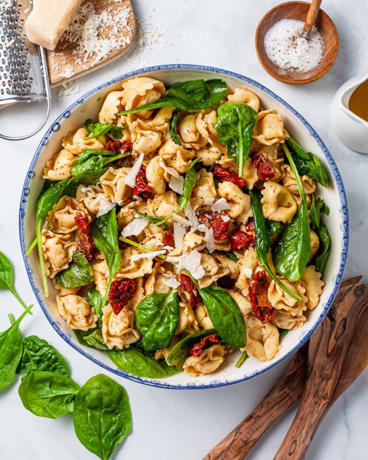 a bowl filled with pasta and spinach next to some bread on a table top