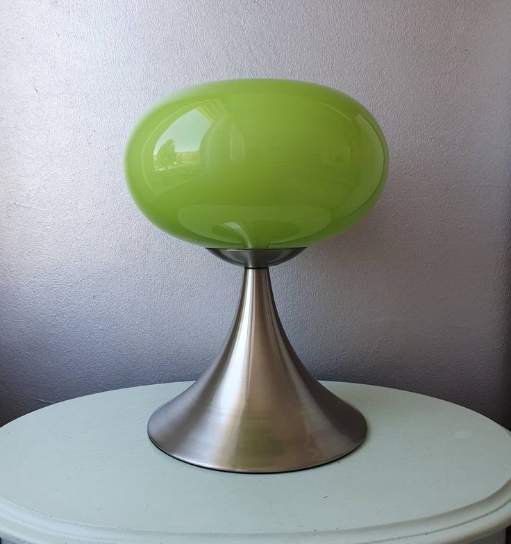 a green lamp sitting on top of a white table next to a gray and purple wall