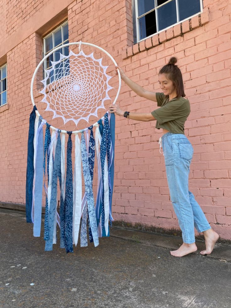 a woman holding up a large white and blue dream catcher in front of a brick building