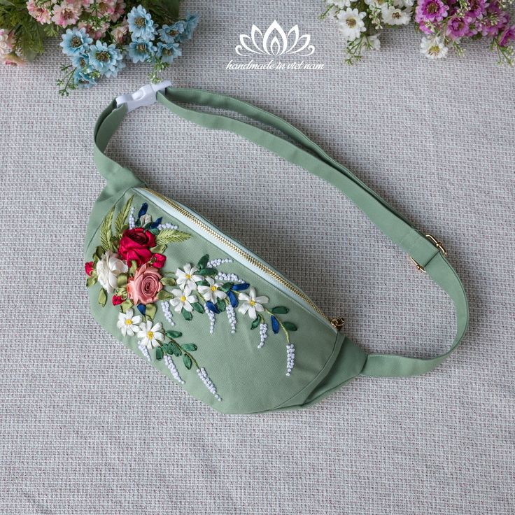 a green purse with flowers on it sitting on a table next to blue and white flowers