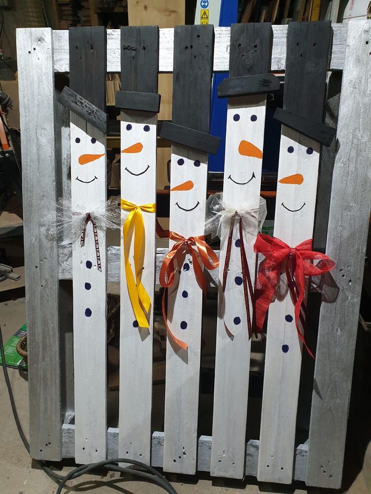 three snowmen made out of wooden pallets with ribbons on them and bows tied around their necks