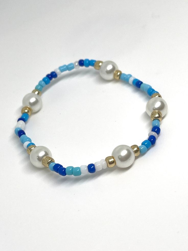 a blue and white beaded bracelet with gold accents on it's end, sitting on a white surface