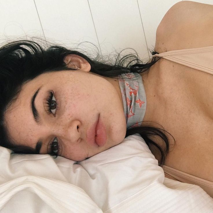 a woman laying on top of a bed next to a white wall and wearing a bra