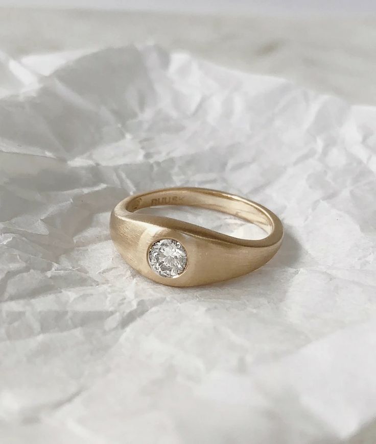 a gold ring with a single diamond on it sitting on top of white tissue paper